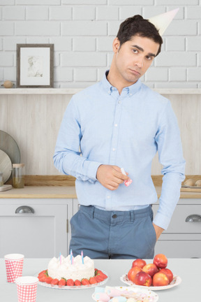 Sad man in party hat standing near birthday cake