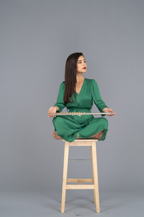 Full-length of a young lady holding her clarinet on her knees while sitting on a wooden chair