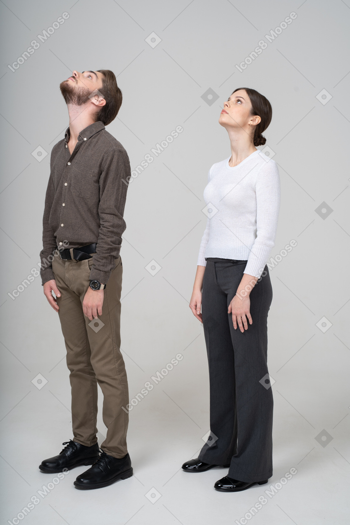 Vista de tres cuartos de una pareja joven en ropa de oficina mirando hacia arriba
