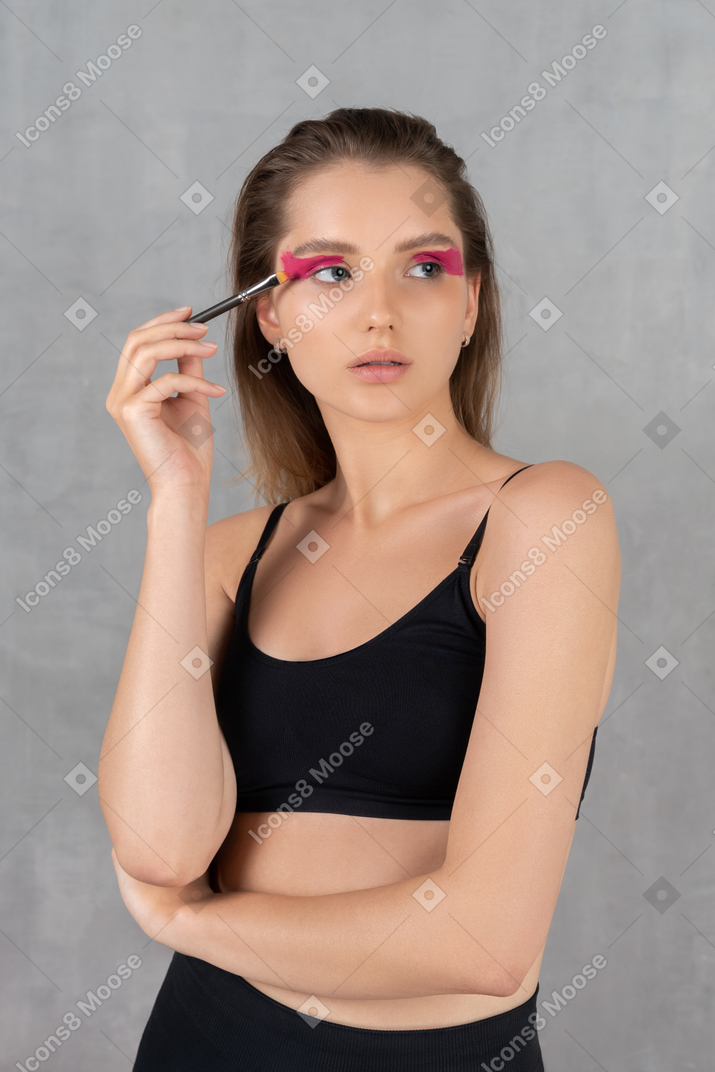 Mujer joven atractiva poniéndose sombra de ojos rosa brillante