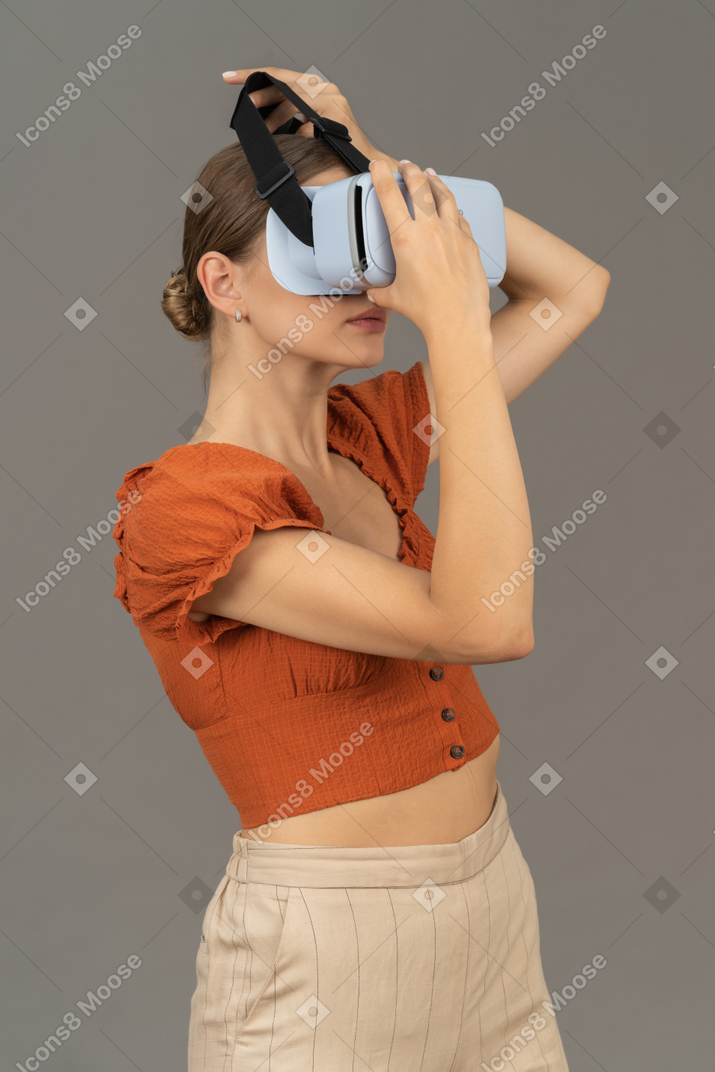 Вид в три четверти на молодую женщину, надевающую виртуальную гарнитуру