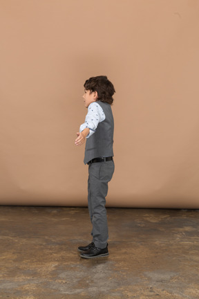 Vista laterale di un ragazzo vestito in piedi con le braccia tese