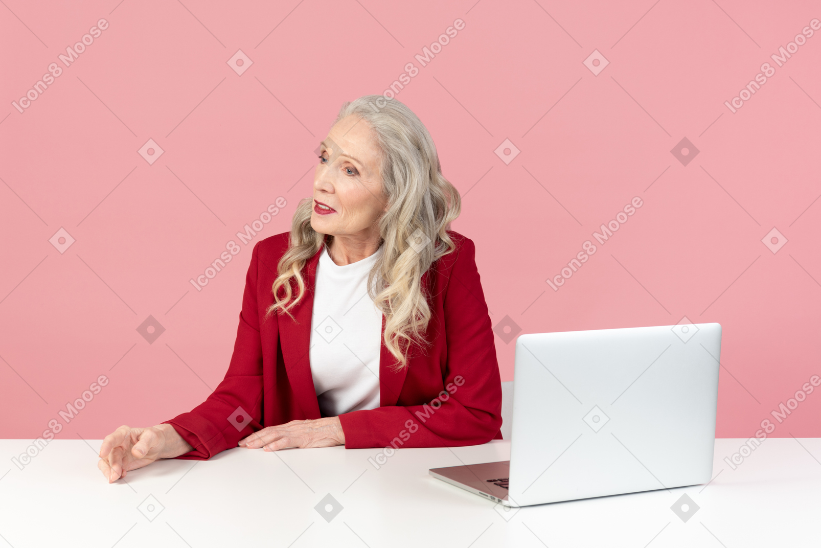 Mujer elegante envejecida sentada en el escritorio de la computadora y mirando a un lado
