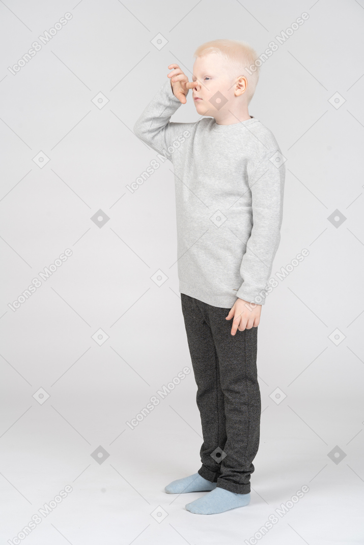 Three-quarter view of a grimacing kid boy touching nose