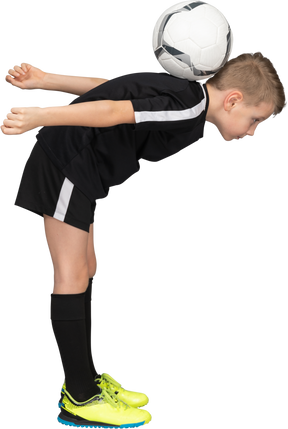 Vista laterale di un ragazzo bambino in uniforme da calcio sporgendosi in avanti e tenendo la palla sulla schiena