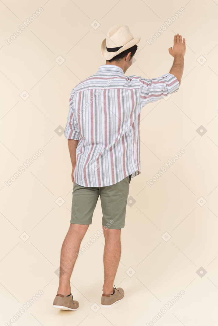 Young caucasian guy standing back to camera with hand up