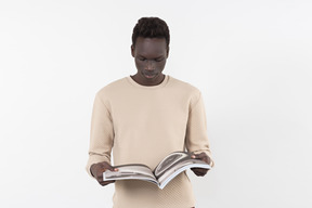 A young black man in a grey sweater standing alone on the white background with a book in his hands