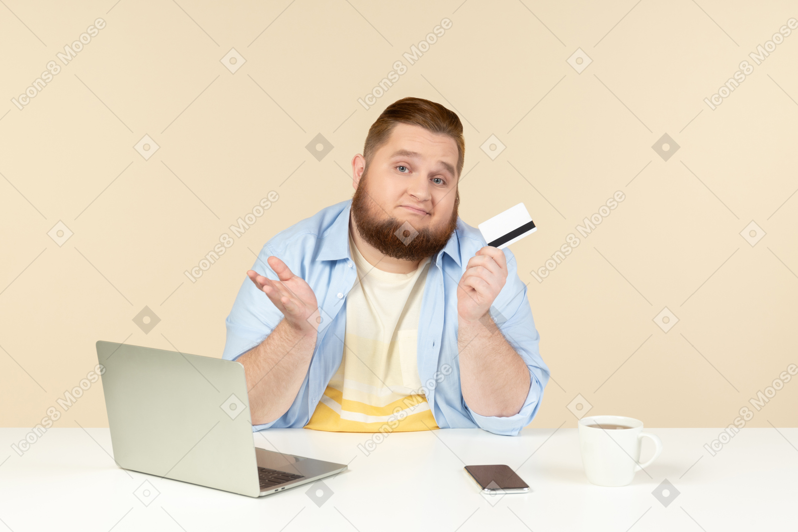 Грустный молодой человек с избыточным весом сидит за столом и держит банковскую карту