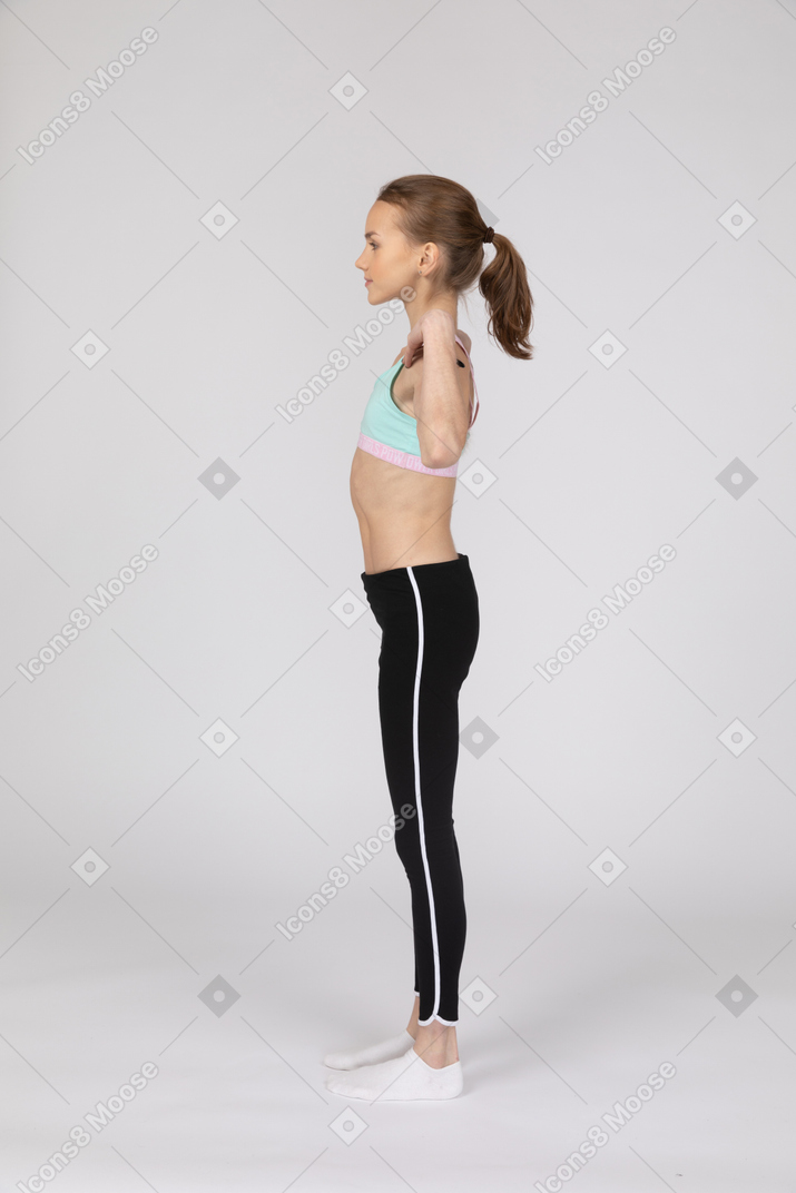 Vista lateral de una jovencita en ropa deportiva tocando sus hombros