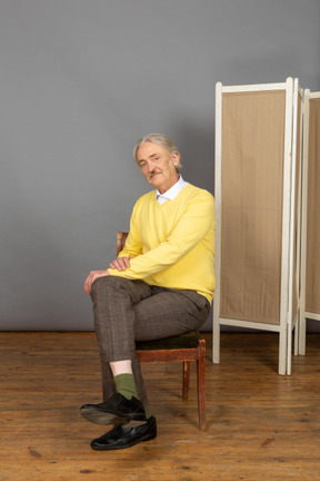 Homem sorridente sentado de pernas cruzadas na cadeira