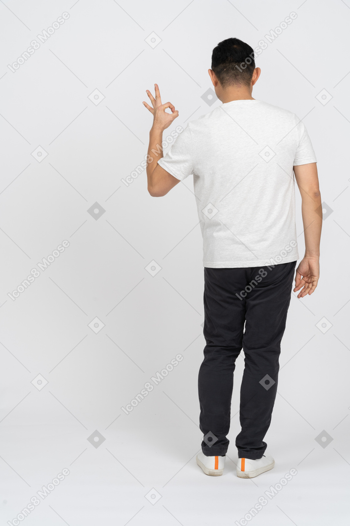 Mann in lässiger kleidung, der zurück zur kamera steht und ein ok-zeichen zeigt