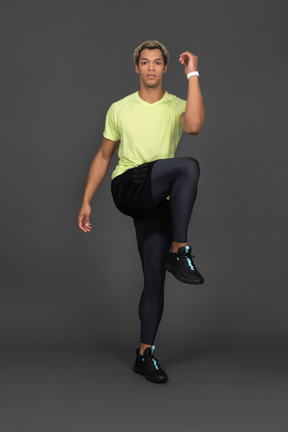 Front view of a dark-skinned young man bending knee and raising leg