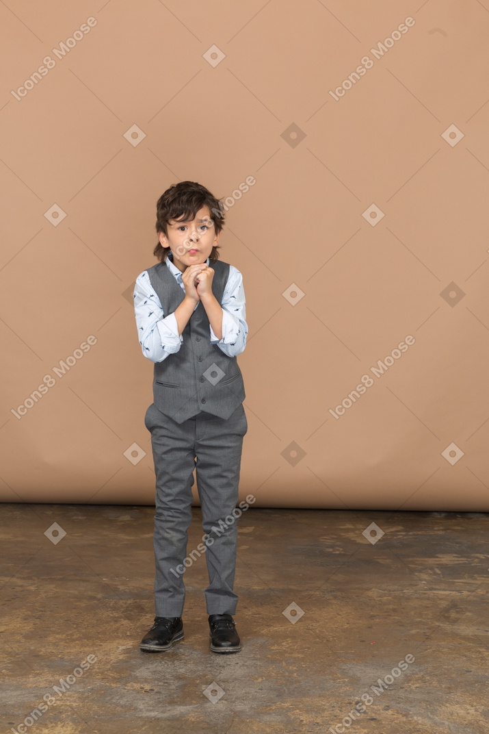 Vorderansicht eines süßen jungen im grauen anzug, der eine betende geste macht