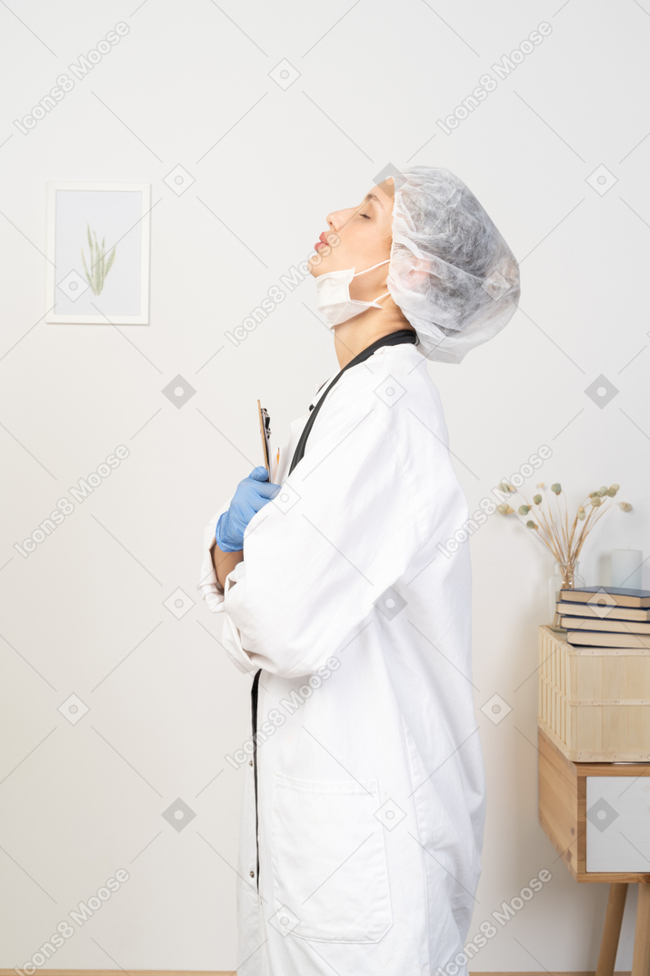 Side view of a sleepy young female doctor holding pencil and tablet