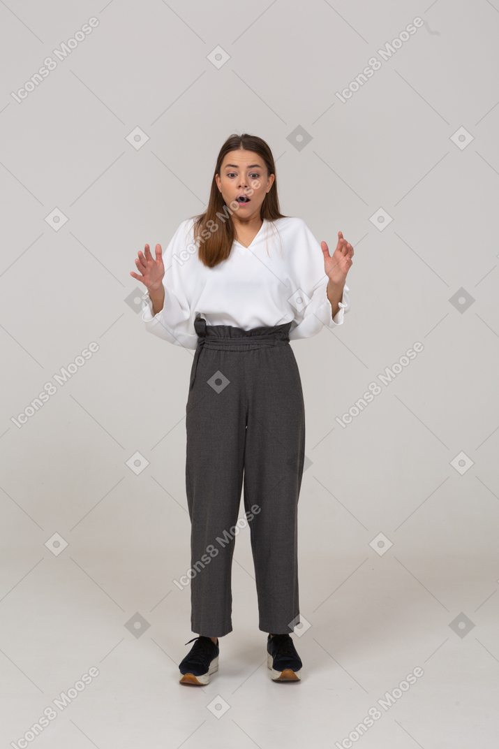 Front view of a shocked young lady in office clothing raising hands