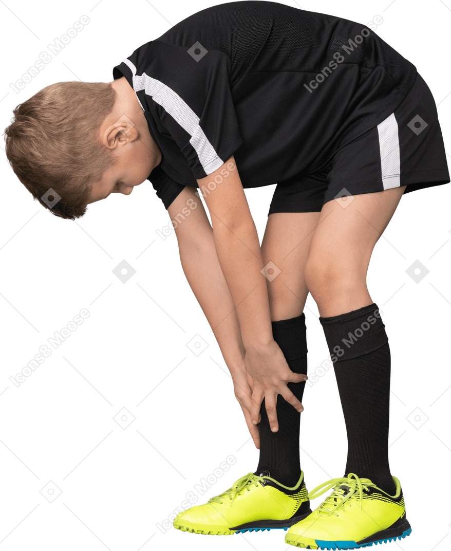 Vista de três quartos de uma criança menino em uniforme de futebol, inclinando-se para a frente e tocando na ponta dos pés