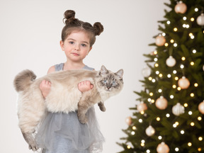 A little girl holding a cat in front of a christmas tree