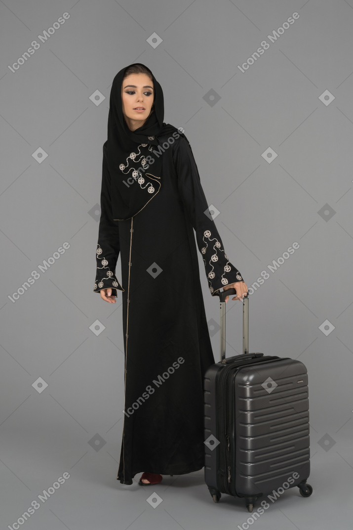 Una mujer musulmana cubierta de pie con una bolsa de equipaje