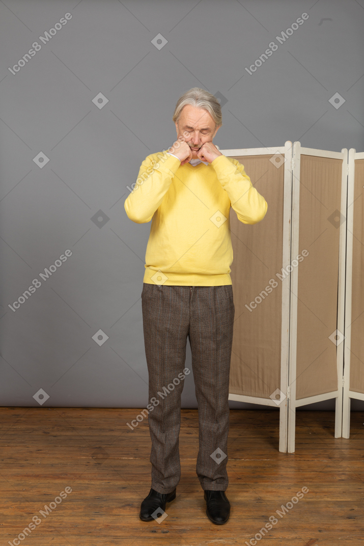 Front view of an old man clenching fists and touching face