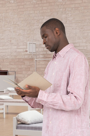 A man standing in a room with beds holding a spiral notebook