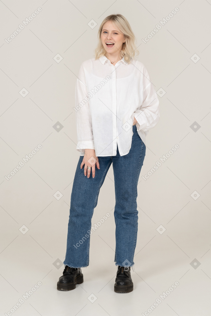Vista frontal de uma jovem sorridente em roupas casuais, colocando as mãos no bolso e piscando