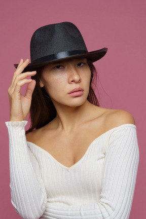 Front view of a bossy young female elegantly touching her black hat