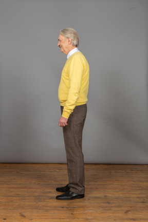 Vista lateral de um homem velho e alegre de blusa amarela sorrindo e olhando para o lado
