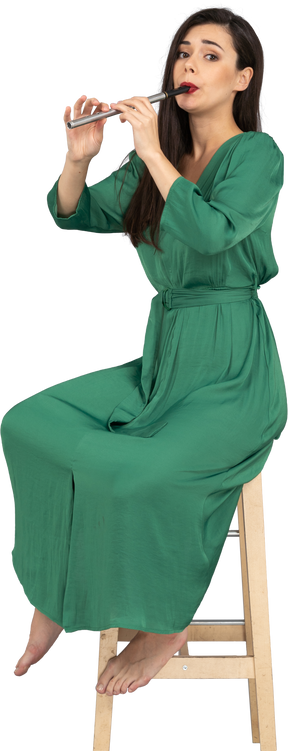 클라리넷을 연주하는 동안 의자에 앉아 녹색 드레스를 입은 젊은 아가씨의 전체 길이