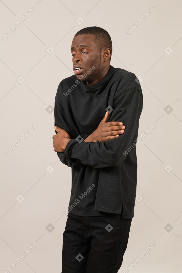 Man in black clothes hugging himself trying to warm up