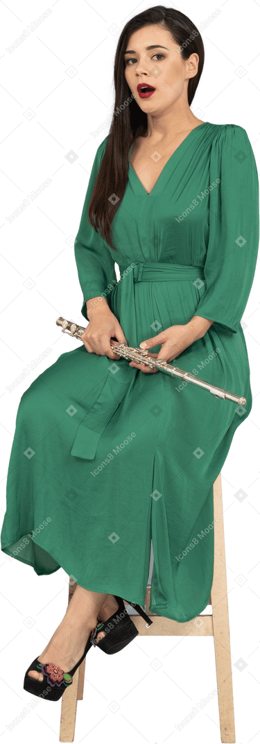 Three-quarter of a surprised young lady in green dress sitting on a chair with a clarinet
