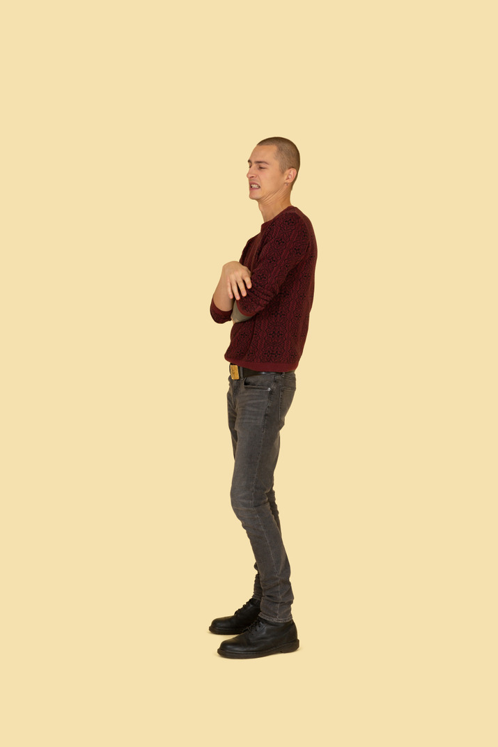 Side view of a displeased young man dressed in casual clothes crossing his hands