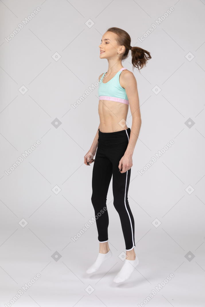 Vista lateral de uma adolescente em roupas esportivas agachada e colocando as mãos nos quadris