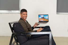 Side view of young man sitting on a sofa and holding a laptop