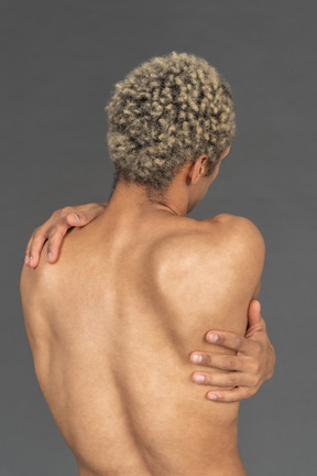 Back view of a shirtless man wrapping his arms around himself
