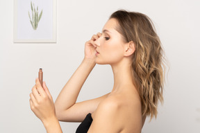 Side view of a young woman wearing black top holding brushing her eyebrows