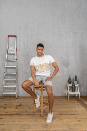 Vue de face du jeune homme assis sur une chaise et regardant la caméra