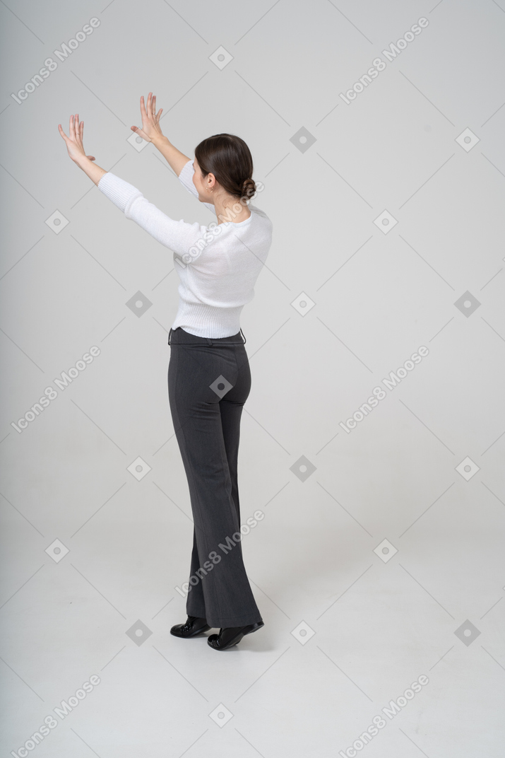 Vista lateral de una mujer con pantalón negro y blusa blanca de pie con los brazos levantados
