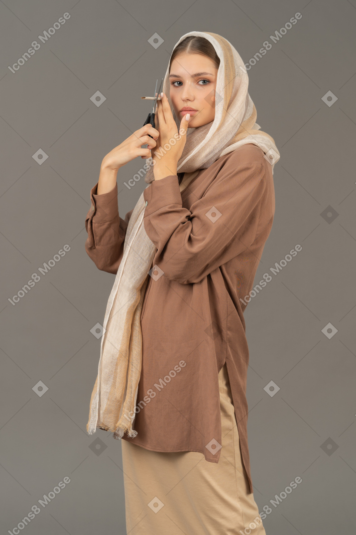 Young woman in beige clothes cutting a cigarette with scissors