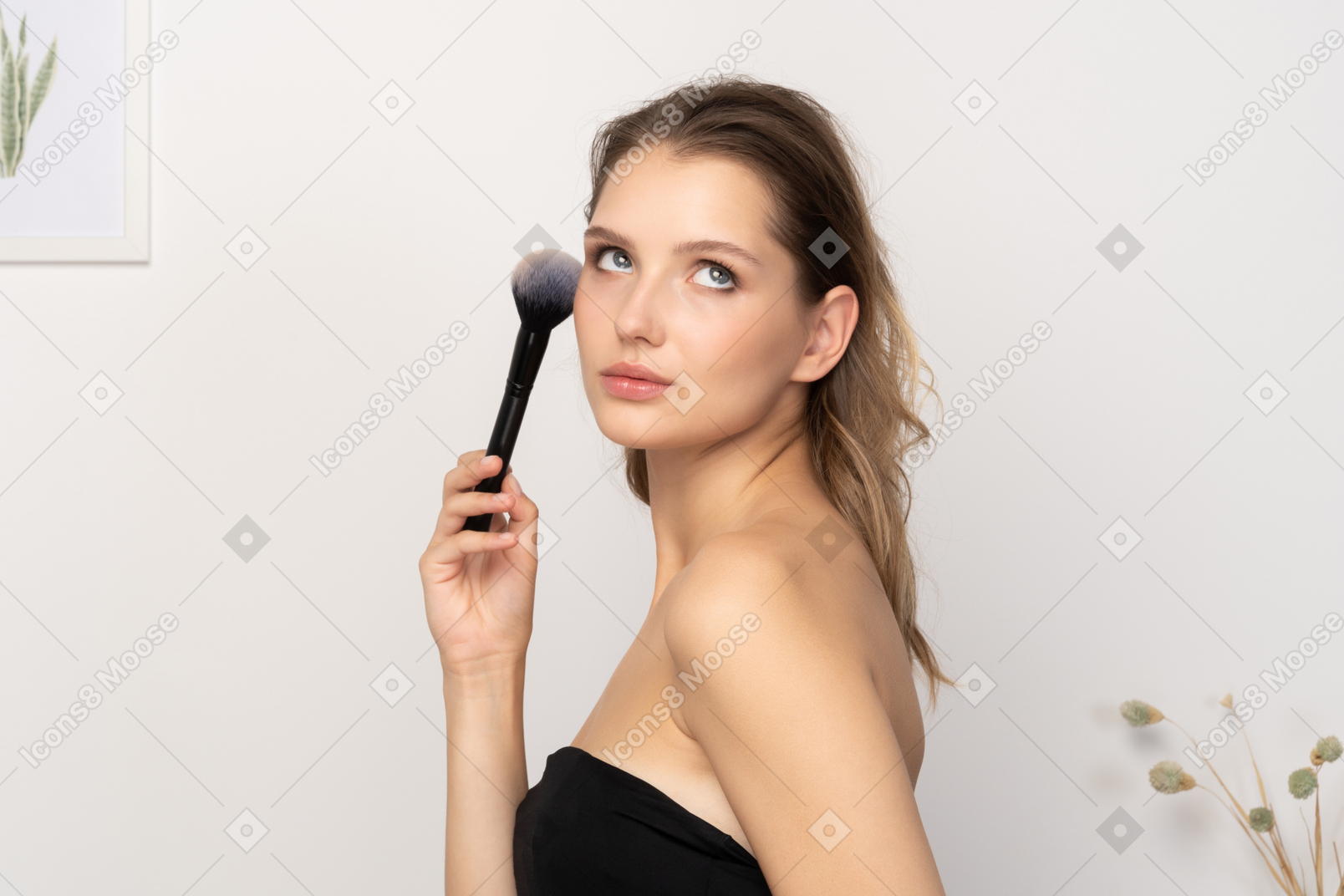 一个性感的年轻女子拿着化妆刷 & 看着相机的侧视图