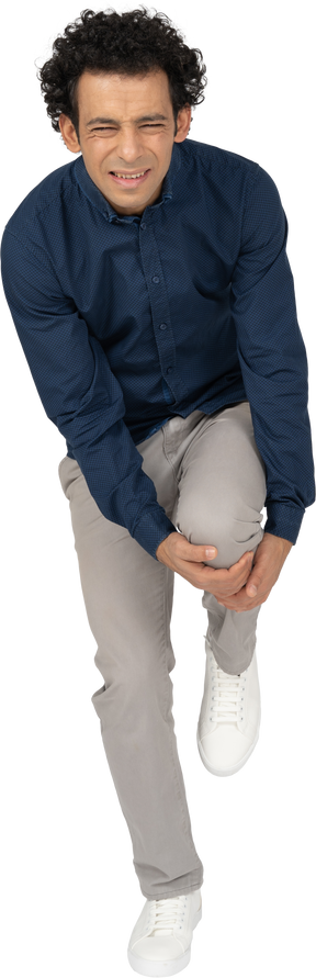 Vista frontal de um homem com roupas casuais tocando o joelho machucado