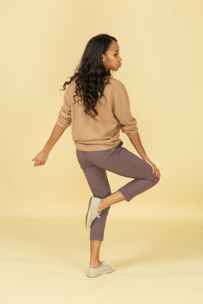 Вид сзади в три четверти темнокожей молодой женщины, касающейся ее колена