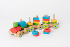 A colorful wooden toy train and geometrical shapes of many colors, lying against a plain white background