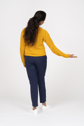 Vista posteriore di una ragazza in abiti casual in piedi con il braccio esteso