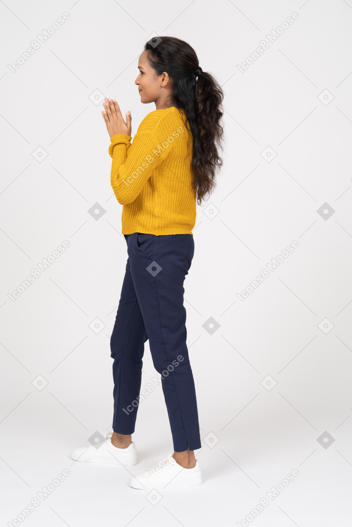 Vista lateral de una niña feliz en ropa casual frotándose las manos