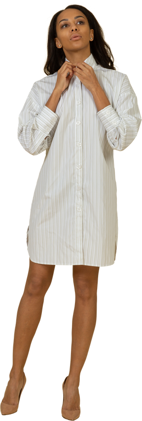 Front view of a dark-skinned young female in white dress adjusting her collar