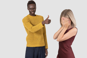 Man showing thumbs up and woman covering face with her hands