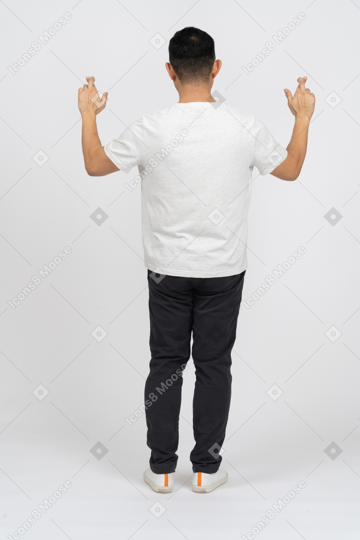 Back view of a man in casual clothes standing with raised hands and crossed fingers