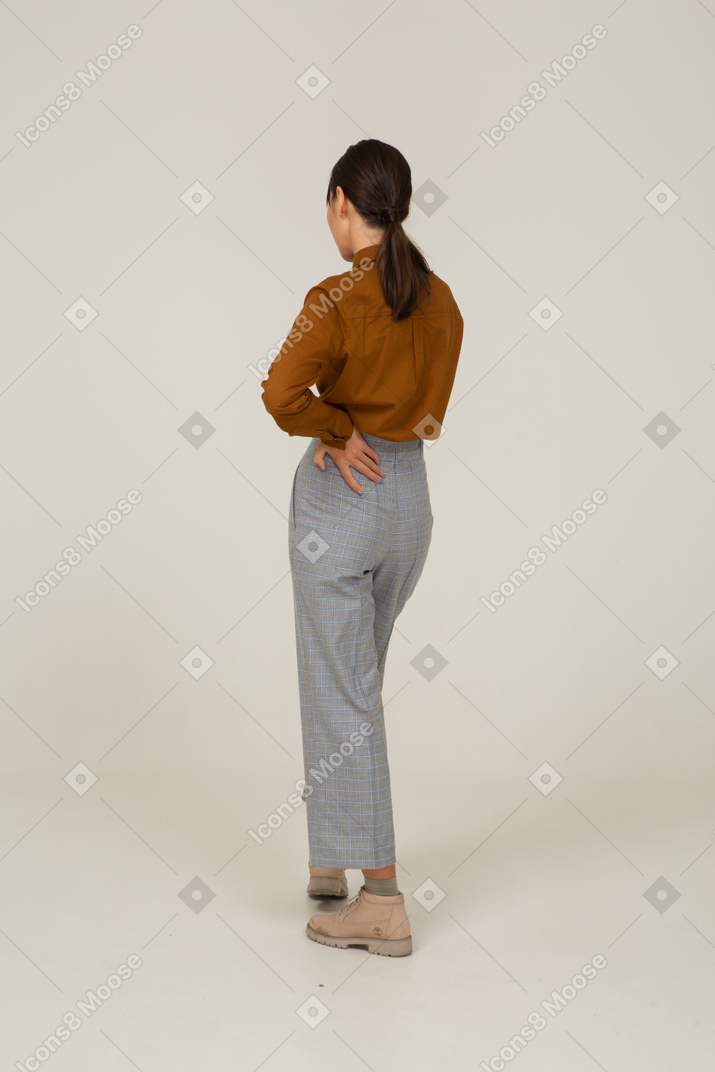 Vista posterior de tres cuartos de una joven mujer asiática en calzones y blusa poniendo la mano en la cadera