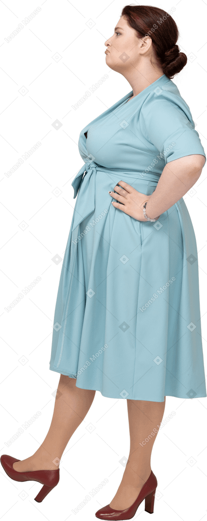 Side view of a woman in blue dress standing with hands on hips
