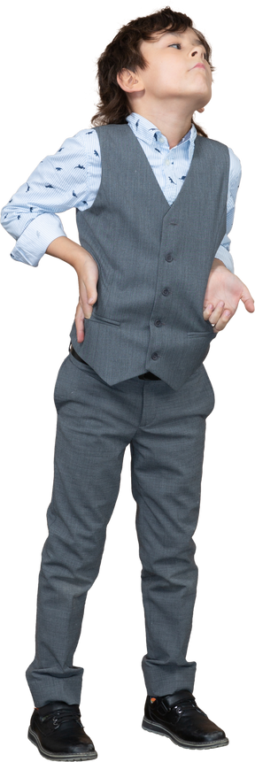 Vorderansicht eines süßen jungen im grauen anzug, der mit der hand auf der hüfte posiert und nach oben schaut